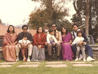 Ajay 'Dadu' Rungta and wife Ma with their extended family (sons, wives, grandkids) in an outdoor group photo on a bench.