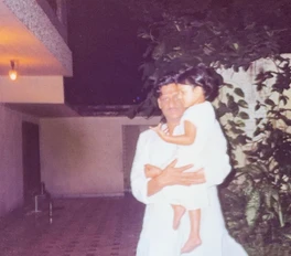 Ajay Rungta (Dadu) in white, holding young Chinu (2 years old) outdoors at night. He looks at the camera.