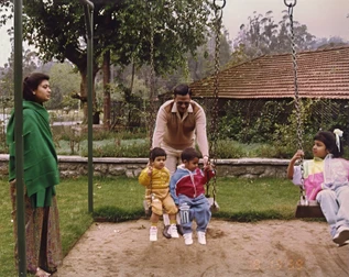 Ajay 'Dadu' Rungta pushes two grandchildren on a swing in a garden. Another child and a woman are present. Dated 1989.