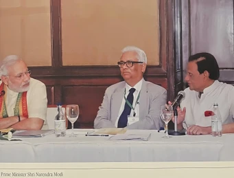 Ajay Rungta in a suit and tie, seated between Prime Minister Narendra Modi and another man at a conference table.