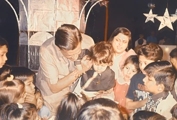 Sepia photo: Ajay 'Dadu' Rungta with grandson Bhaiya at his 1st birthday party. Dadu interacts with Bhaiya, children watch.