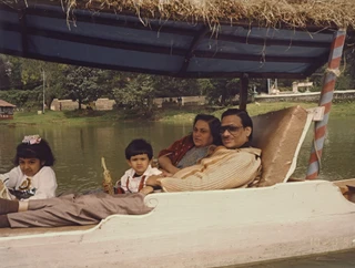 Dadu Ajay Rungta and Ma with two young children, Chinu and Puru, smiling while sitting in a covered boat on a lake.