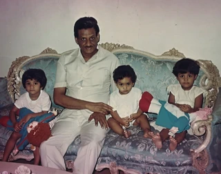 Ajay Rungta (Dadu) sits on an ornate sofa with three young granddaughters: Prerna, Shikha, and Chinky. All look at the camera.