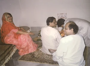 Indoor photo: Ajay Rungta (Dadu), his wife (Ma) in a red saree, and 'Peela Dadu' participating in a Diwali pooja ceremony, seated on a rug.