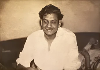 Sepia close-up of young Ajay Rungta (Dadu) smiling warmly. He has dark hair and wears a light open-collar shirt.