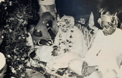 Vintage black and white photo of a traditional Indian wedding. Groom in headdress on right, figures seated during ceremony.