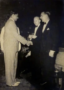 Vintage black and white photo: Ajay Rungta in a light suit shakes hands with George H.W. Bush in a tuxedo at an event.