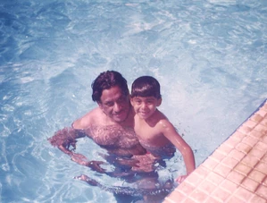 Ajay Rungta (Dadu) and his grandson Aman smiling together in a sunlit swimming pool, capturing a moment of joyful family time.