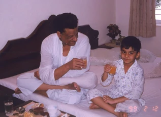 Ajay 'Dadu' Rungta and grandson Aman in pyjamas, smiling on a bed, sharing juice. A breakfast tray is visible.