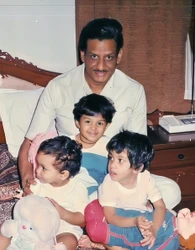 Ajay 'Dadu' Rungta sitting on a bed, smiling, with his three young grandchildren, Prerna, Shikha, and Chinu, around him.