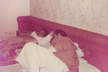 Ajay 'Dadu' Rungta and Peela Dadu relaxing together on a bed. A casual, indoor scene showing a moment of rest.