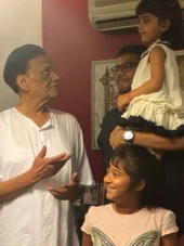 Ajay Rungta (Dadu) in a white top, engaging with his son Aman, who holds one granddaughter. Another granddaughter smiles in the foreground.