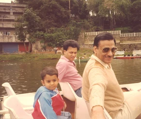 Ajay 'Dadu' Rungta, Kaku, and Bhaiya on a boat. Dadu smiles in the foreground, Kaku and Bhaiya behind him on a lake.