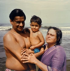 Ajay Rungta (Dadu) in the sea holding grandson Bhaiya, with wife Ma nearby. Sunny family beach portrait.