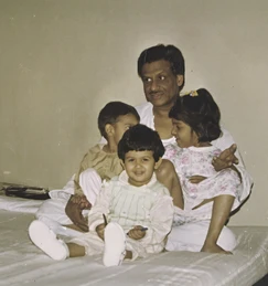 Ajay 'Dadu' Rungta sits smiling with three young grandchildren gathered around him in a warm, indoor setting.