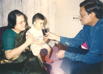 Dadu Ajay Rungta and Ma lovingly offer a drink to their grandson Aman, who sits on Ma's lap.