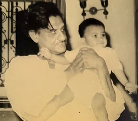 Sepia photo: Ajay 'Dadu' Rungta smiling while holding a young child, Chinu, in his arms indoors.
