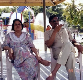 Ajay Rungta (Dadu) and his wife (Ma) relaxing outdoors at a waterpark in 1999. Both are seated; Dadu wears sunglasses and gestures.