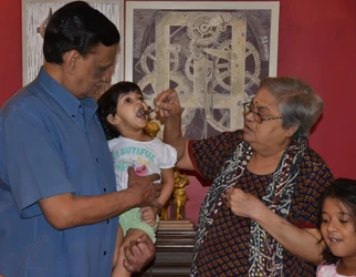 Ajay Rungta (Dadu) holds his grandchild. The child is being spoon-fed by their grandmother. Another child watches.