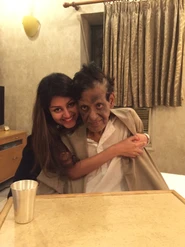 Ajay Rungta (Dadu) seated and smiling, lovingly embraced by a younger woman, Chinu, in a warm indoor setting.
