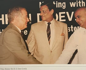 Ajay Rungta shaking hands with former Indian Prime Minister H. D. Deve Gowda at an event. Another person is partially visible.