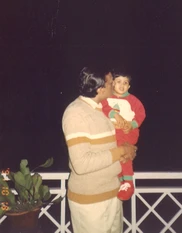 Ajay 'Dadu' Rungta kisses grandchild Popo. Dadu wears a beige sweater; Popo red pajamas. Nighttime balcony scene.